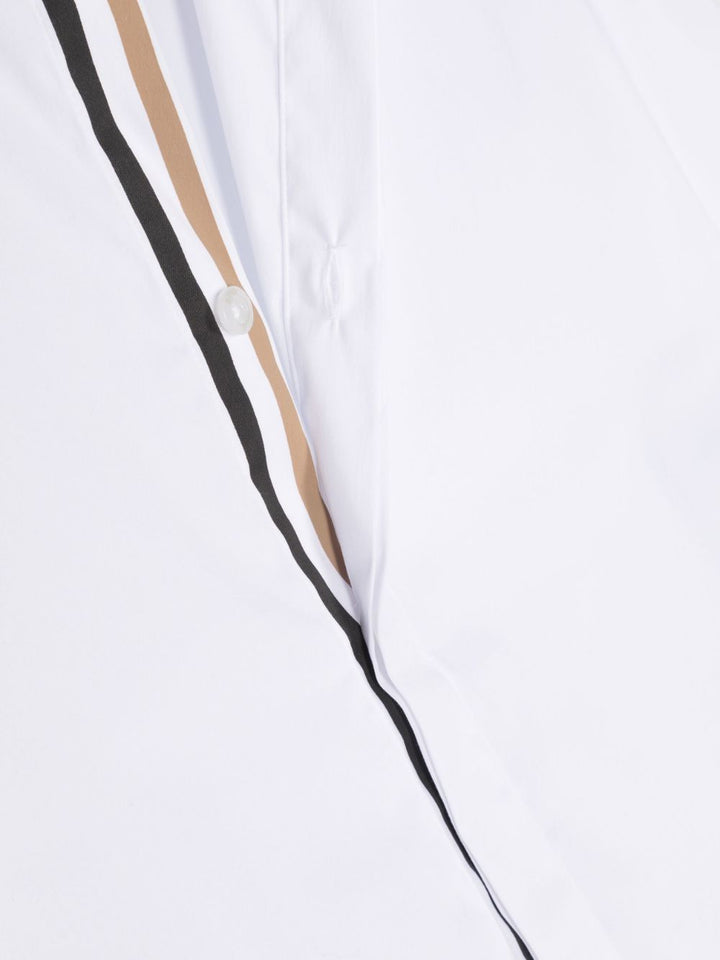 Chemise garçon blanche, col pointu, manches longues, bas boutonnés, bord rayé, fermeture boutonnée cachée sur le devant et bas arrondi