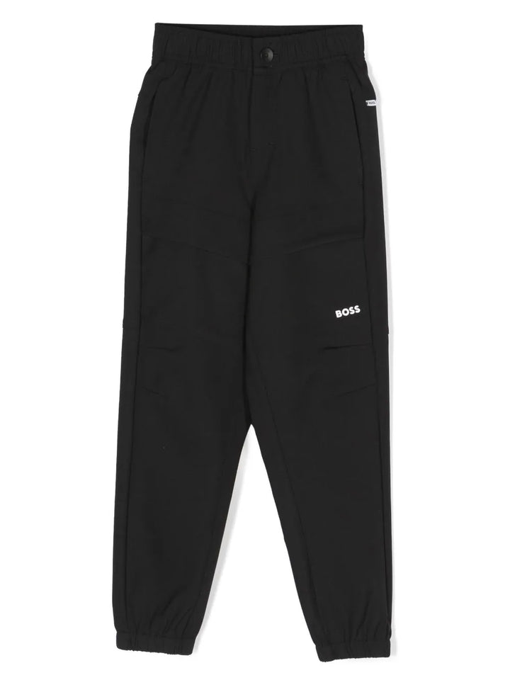 Pantalon de sport noir et blanc pour enfant, détail plissé, logo imprimé sur la jambe, taille haute, fermeture sur le devant avec boutons et zip, deux poches latérales en biais et poignets élastiqués